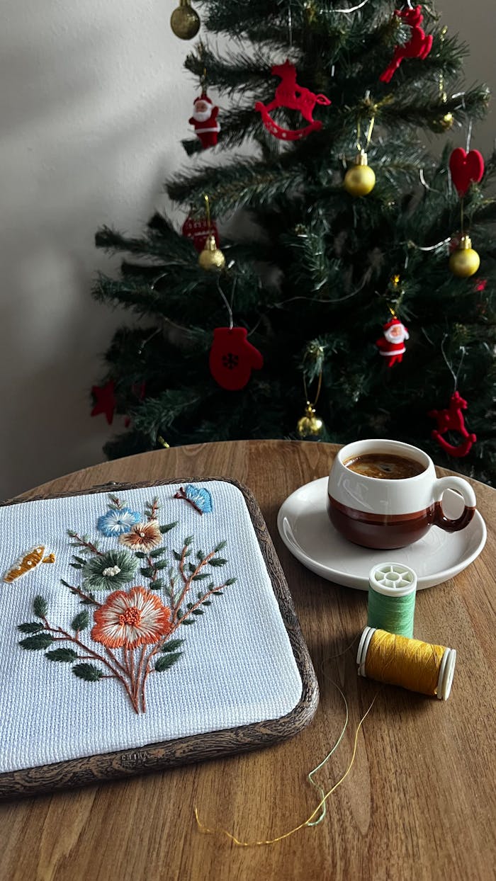 Handcrafted embroidery and espresso by a Christmas tree create a warm holiday atmosphere.